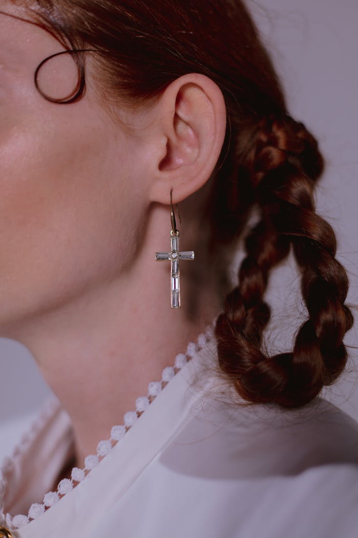 Crafting Captivating Headlines: Your awesome post title goes here A close-up of a cross-shaped earring worn by a woman with braided hair.