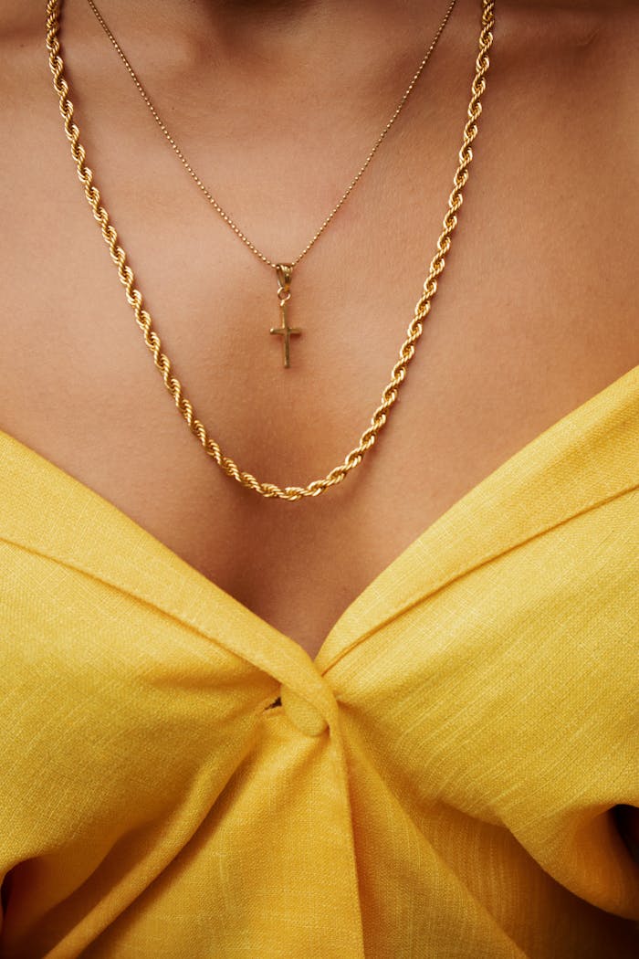 Close-up of a gold cross necklace and yellow attire, showcasing elegance and style.